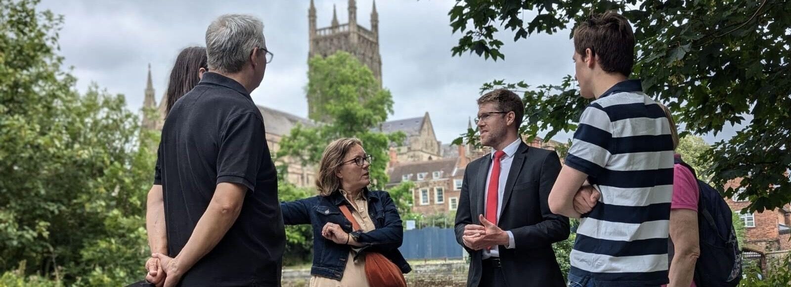 Tom Collins talking to constituents by the river with the cathedral in the background.